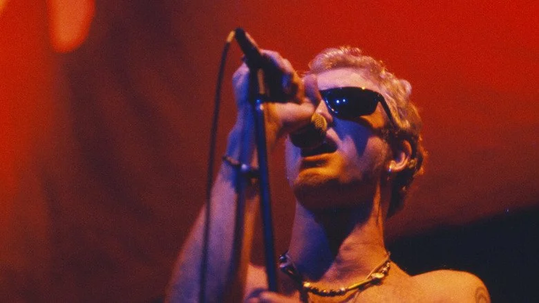 Layne Staley chantant sur scène éclairée en rouge avec des lunettes de soleil