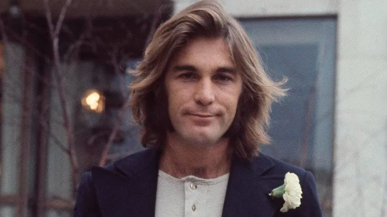 Dennis Wilson souriant dans un blazer sur une photo posée
