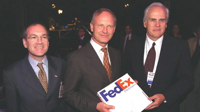 Fred Smith avec deux autres hommes, tenant une boîte FedEx