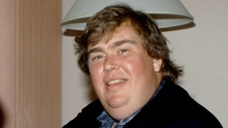John Candy souriant devant une lampe