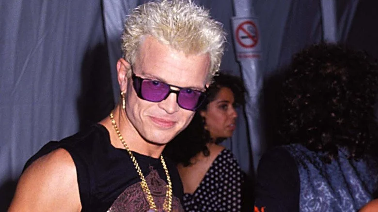 Billy Idol avec des lunettes de soleil violettes souriant à la caméra