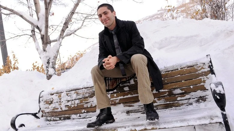Nev Schulman assis sur un banc de parc couvert de neige