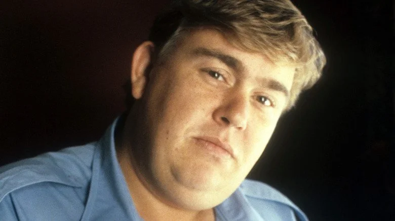 John Candy incliné et regardant sensiblement la caméra