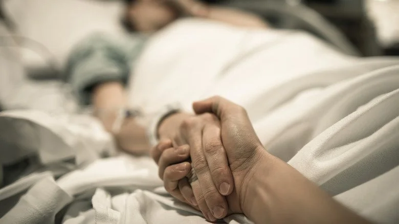 person on sickbed holding visitor's hand