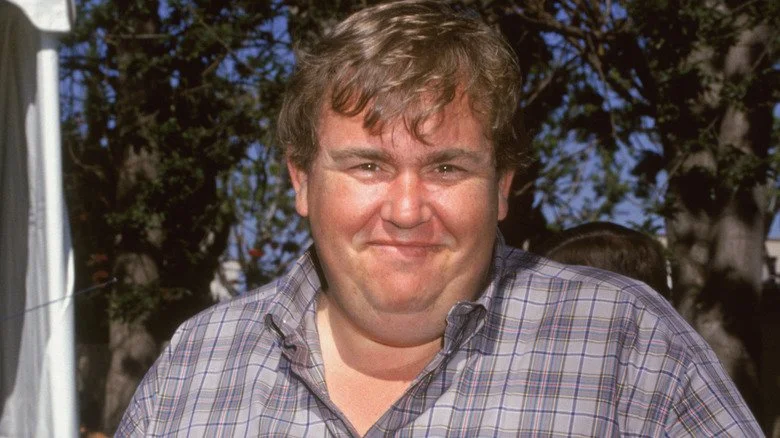 John Candy souriant dans une chemise à carreaux