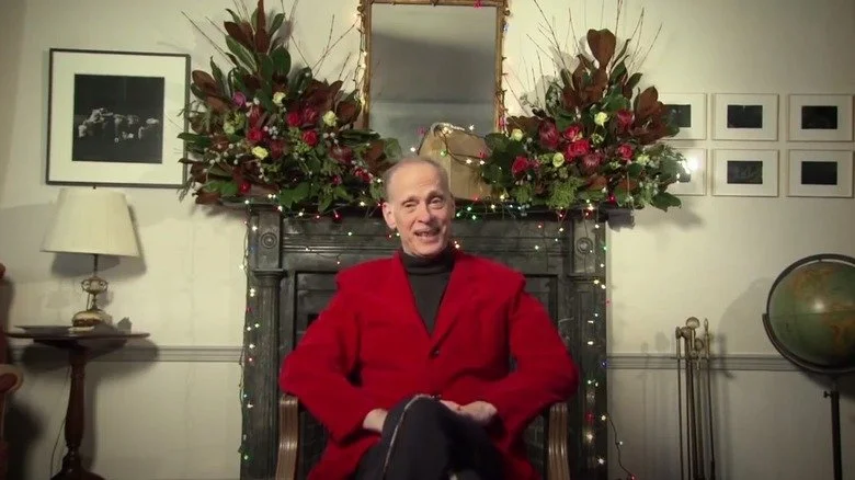 John Waters dans une veste rouge avec des décorations de Noël