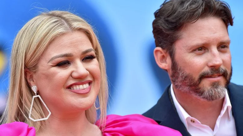 Kelly Clarkson souriante dans une robe rose avec Brandon Blackstock en costume lors d'un événement