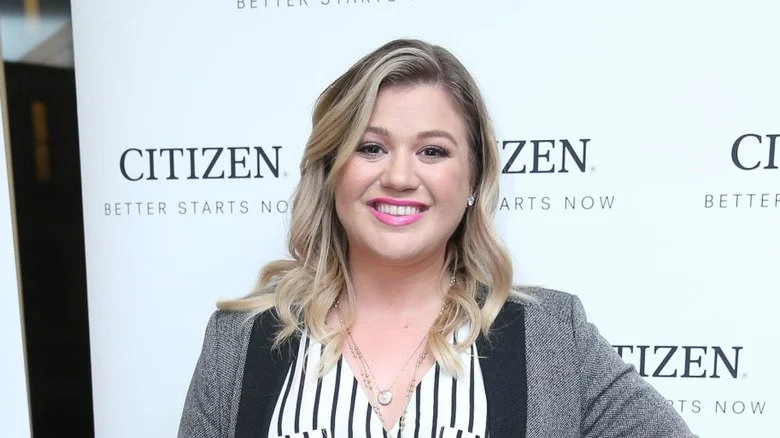 Kelly Clarkson souriant dans un blazer gris lors d'un événement