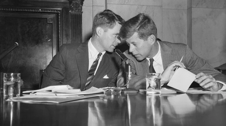 Robert et John F. Kennedy assis à un bureau en train de parler