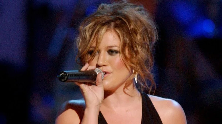 Kelly Clarkson chantant sur scène en robe noire avec des cheveux bouclés