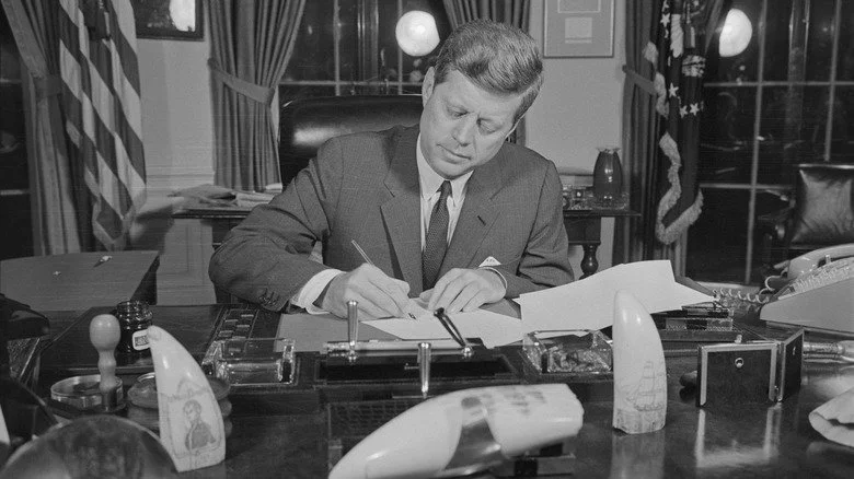 John F. Kennedy signant un document dans son bureau