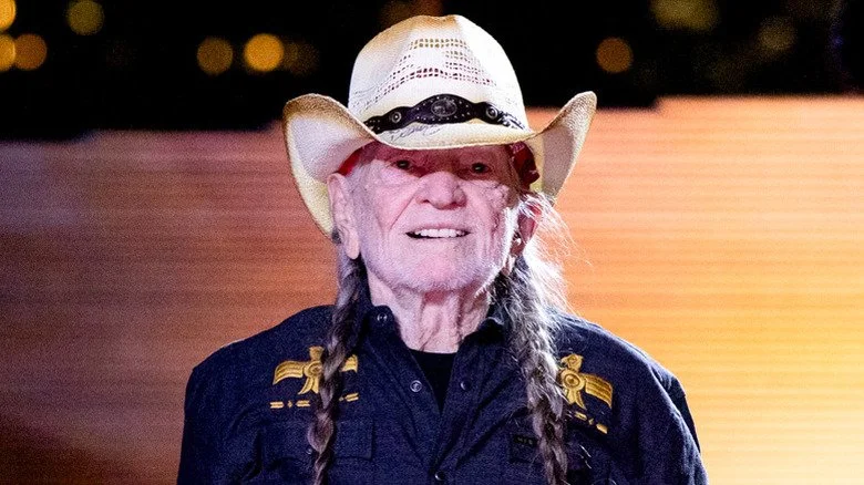 Willie Nelson portant un chapeau et souriant à moitié sur scène