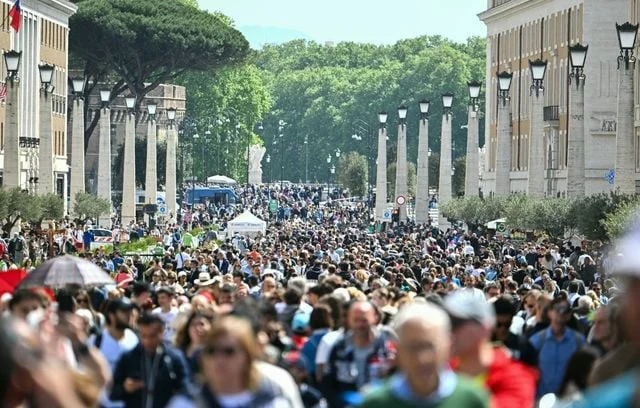 Des fidèles et des pèlerins marchent sur la via della Conciliazione pour se rendre sur la place Saint-Pierre après le décès du pape François, au Vatican.