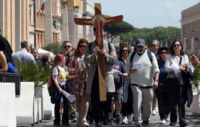 Des pèlerins portant la croix entrent sur la place Saint-Pierre, ce lundi, jour de la mort du pape François.