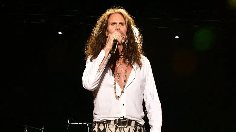 Steven Tyler chantant devant un micro sur fond noir