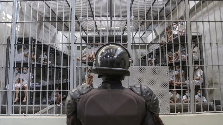 guard stands before cell with prisoner at CECOT