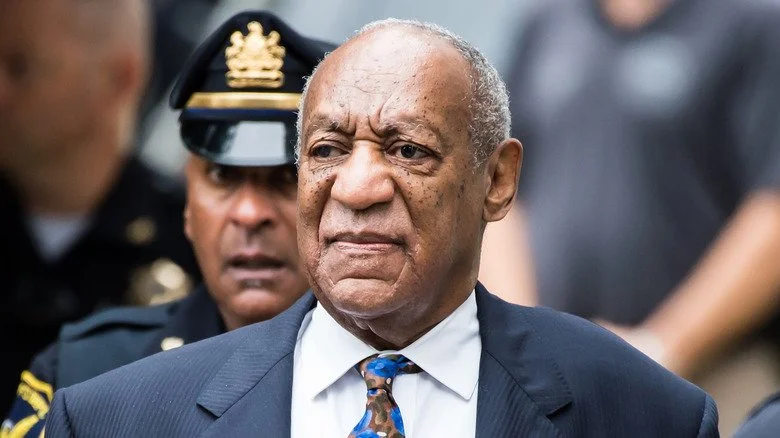 Bill Cosby à l'extérieur du tribunal, avec un policier derrière lui