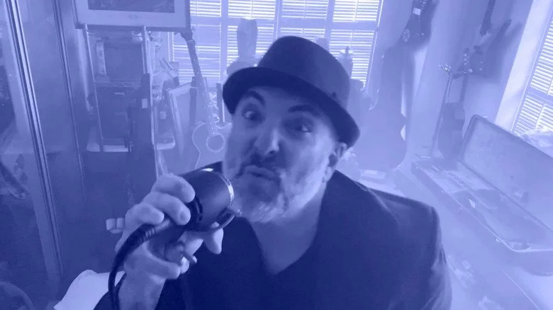 Brian Tutunick chantant dans un clip musical, portant un petit chapeau noir