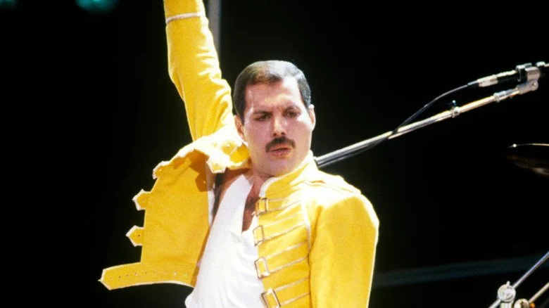 Freddie Mercury en veste jaune levant le bras