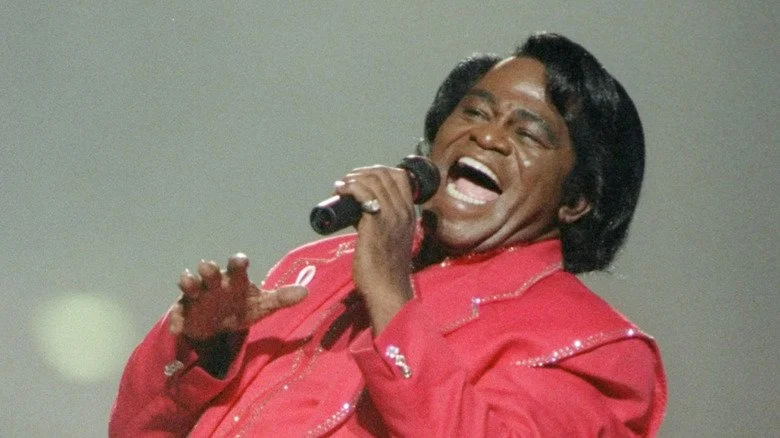 James Brown chantant énergiquement sur scène en costume rouge