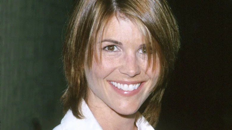 Lori Loughlin souriante avec une frange et une chemise blanche dans les années 90