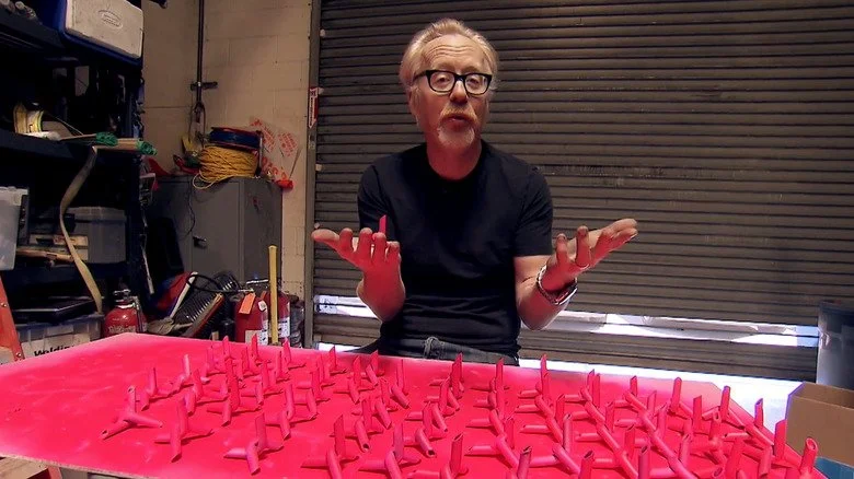 Adam Savage devant des pics de route peints en rose