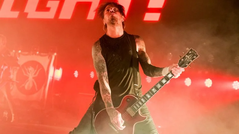 Rob Holliday jouant de la guitare sur une scène éclairée en rouge