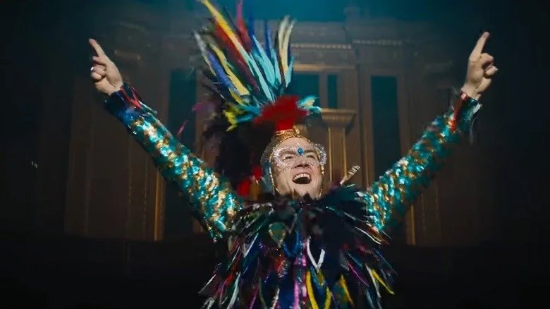Taron Egerton as Elton John arms raised in costume in a scene from Rocketman