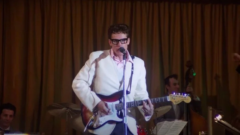 Gary Busey as Buddy Holly in white suit playing guitar onstage in a scene from The Buddy Holly Story