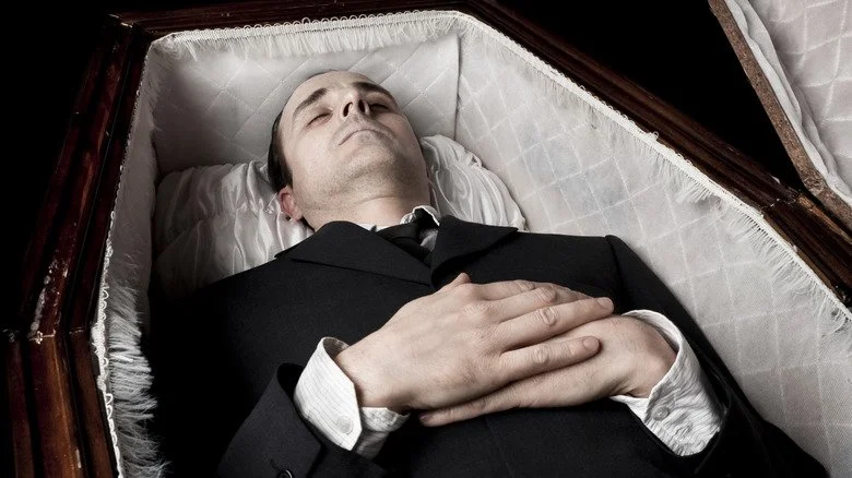 Personne allongée dans un cercueil avec les mains sur l'abdomen