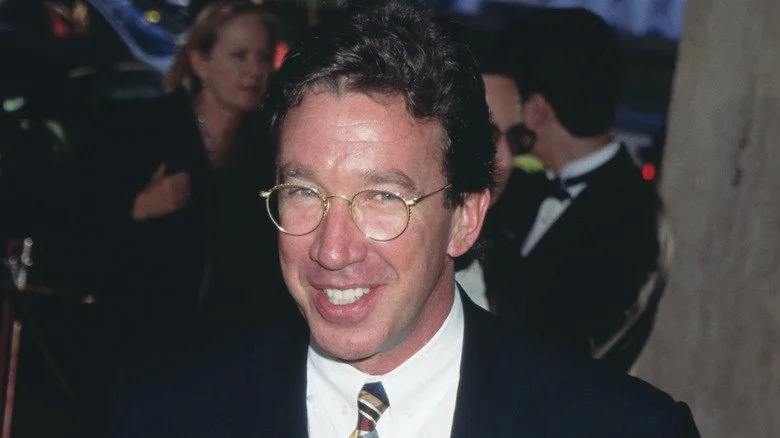Tim Allen souriant avec des lunettes lors d'un événement des années 90