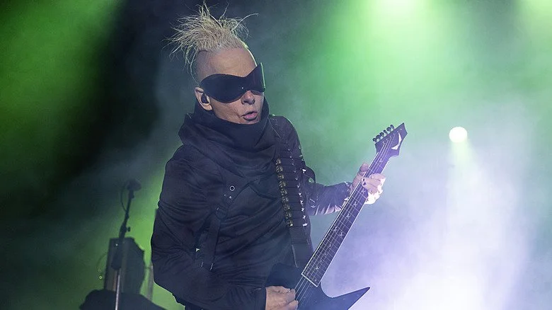 Tim Skold jouant de la guitare sur scène avec des lunettes de soleil enveloppantes