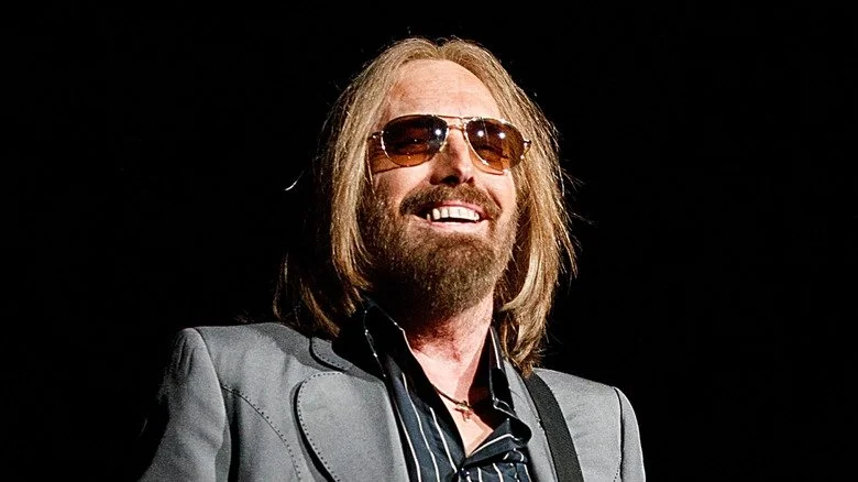 Tom Petty souriant sur scène dans un costume gris