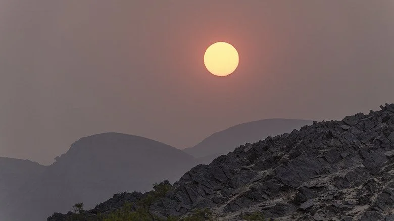 Soleil derrière des nuages de poussière, crêtes rocheuses au premier plan