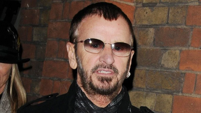 Ringo Starr faisant une grimace devant un mur en briques