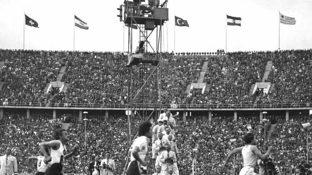 Des coureurs lors des Jeux Olympiques d'été de 1936, avec les drapeaux nationaux flottant au sommet du stade.