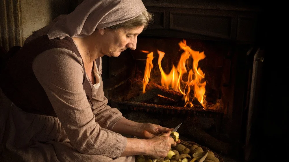 Portrait d’une paysanne médiévale épluchant des pommes de terre près de son foyer