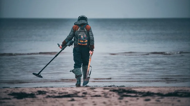 Un homme avec un détecteur de métaux et une pelle sur la plage