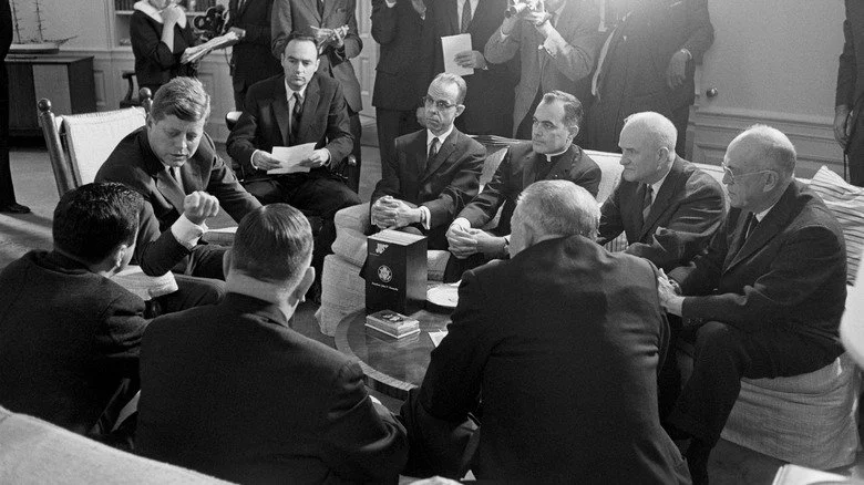 Kennedy assis avec des assistants et des législateurs entourés de photographes