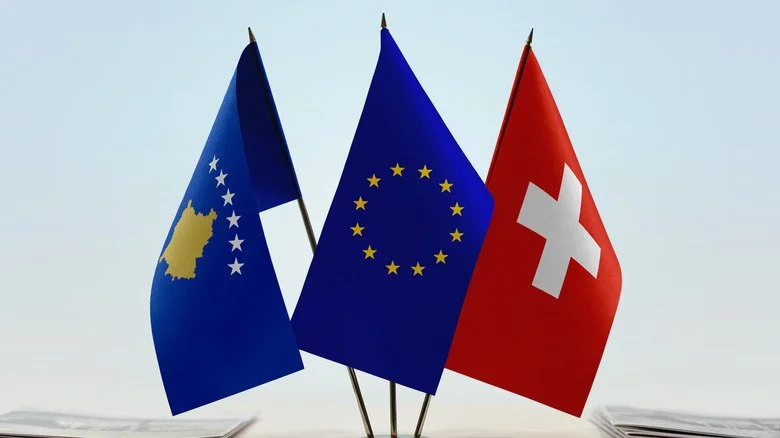Drapeaux du Kosovo, de l'UE et de la Suisse sur un bureau avec des documents