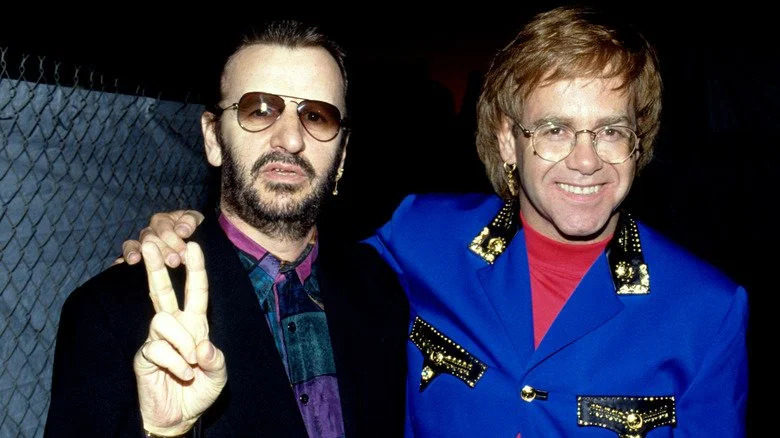 Ringo Starr faisant le signe de la paix avec Elton John souriant