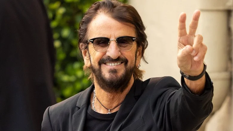 Ringo Starr souriant et faisant le signe de la paix