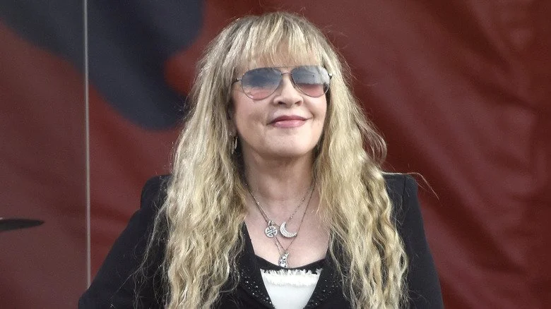 Stevie Nicks souriante avec des lunettes de soleil sur scène en extérieur