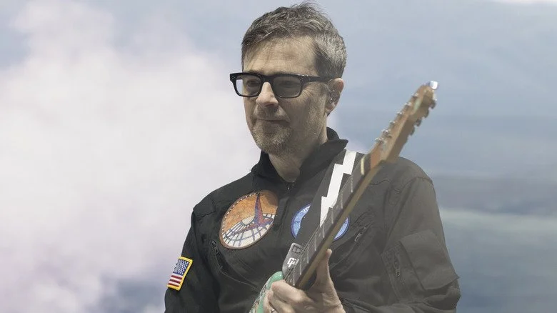 Rivers Cuomo regardant tristement en jouant devant des nuages