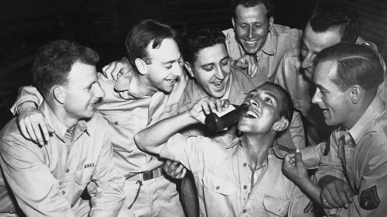 Soldats riant tandis qu'un autre verse une bière dans sa bouche