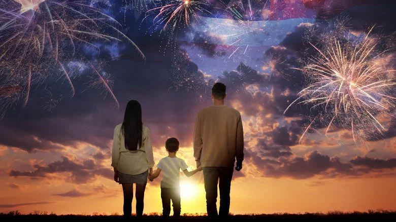 Famille debout devant un horizon avec un ciel illuminé par des feux d'artifice