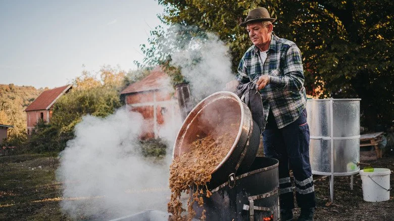 Homme versant un pot d'ingrédients de distillation maison en plein air