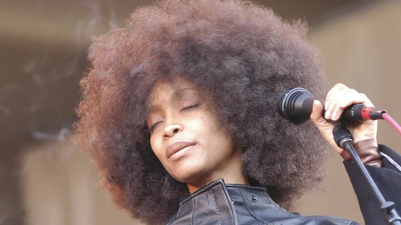 Erykah Badu les yeux fermés avec un micro sur scène