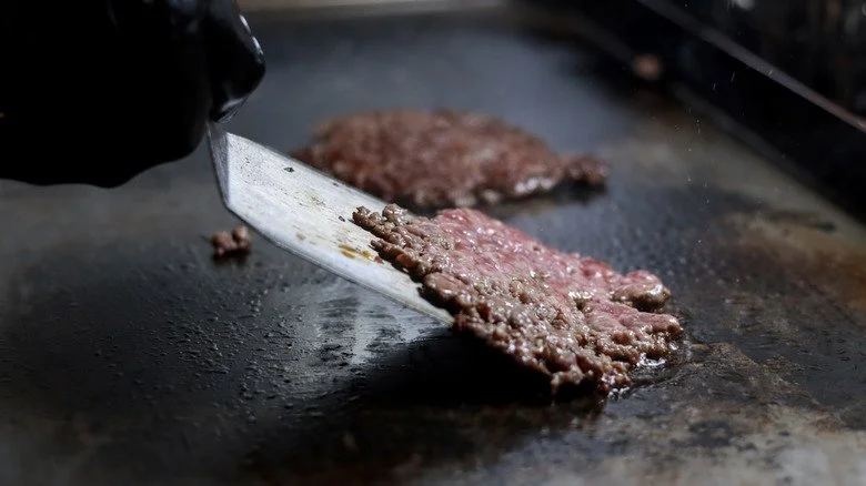 Une main gantée retourne un burger avec une spatule