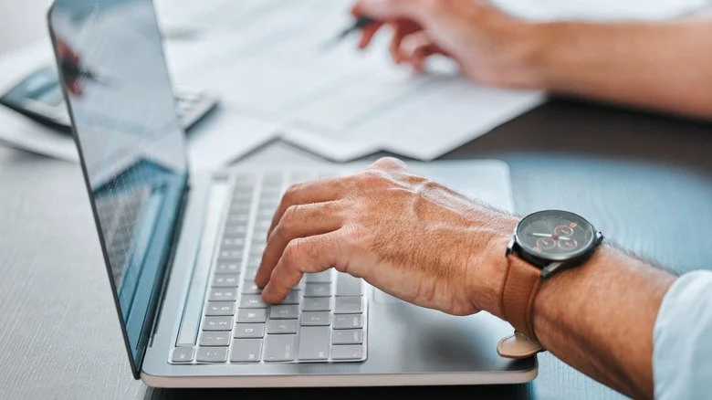 Un homme travaillant sur un ordinateur portable tout en écrivant sur du papier